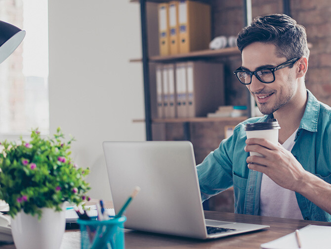 Employee Working on Laptop Smiling With Coffee Cup